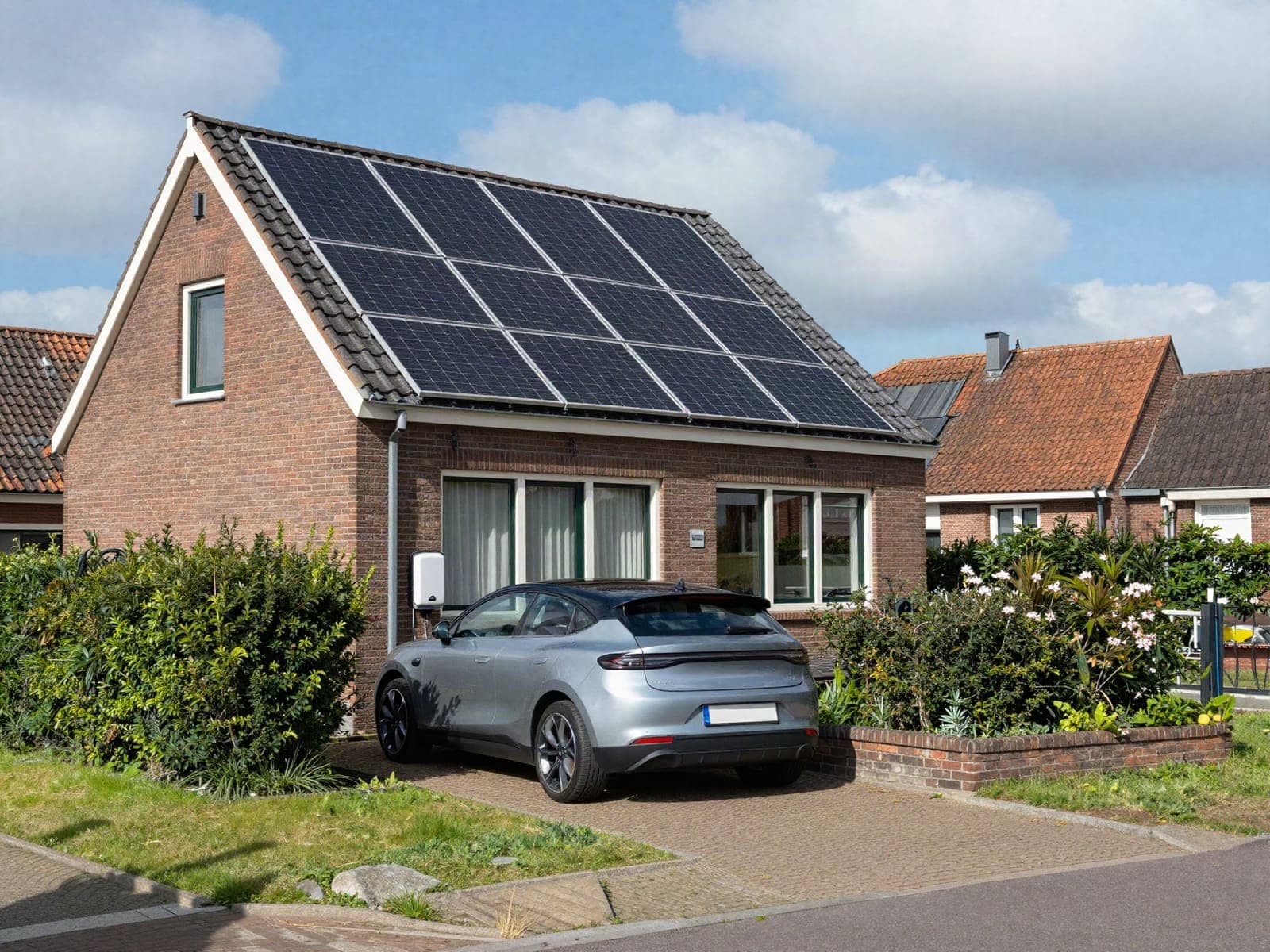 Woning met zonnepanelen op het dak, een elektrische auto op de oprit en een laadpaal aan de gevel